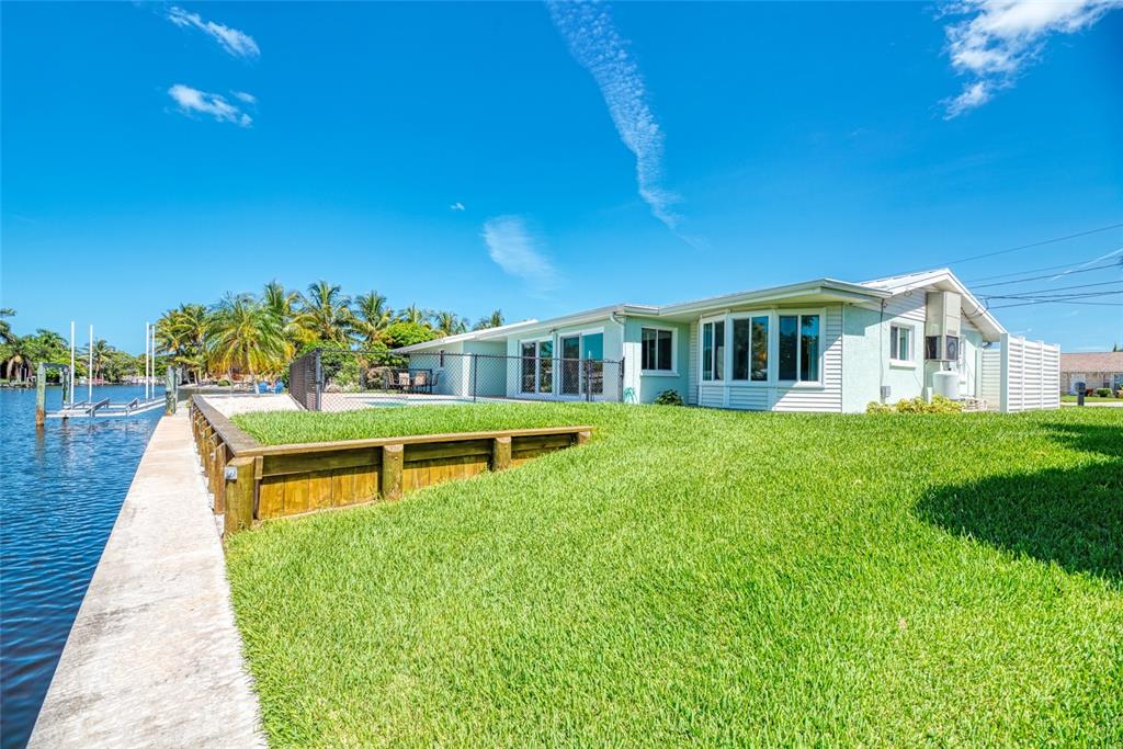 A light-colored house sits on a grassy lot next to a canal with a dock — 5577 CONTENTO DRIVE, SARASOTA, FL