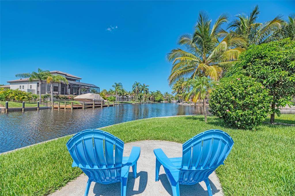 Two blue Adirondack chairs sit on a lawn overlooking a canal with a boat dock — 5577 CONTENTO DRIVE, SARASOTA, FL