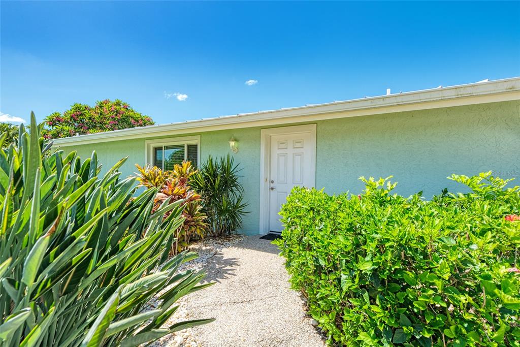 A light green house exterior features a white front door and a gravel walkway — 5577 CONTENTO DRIVE, SARASOTA, FL