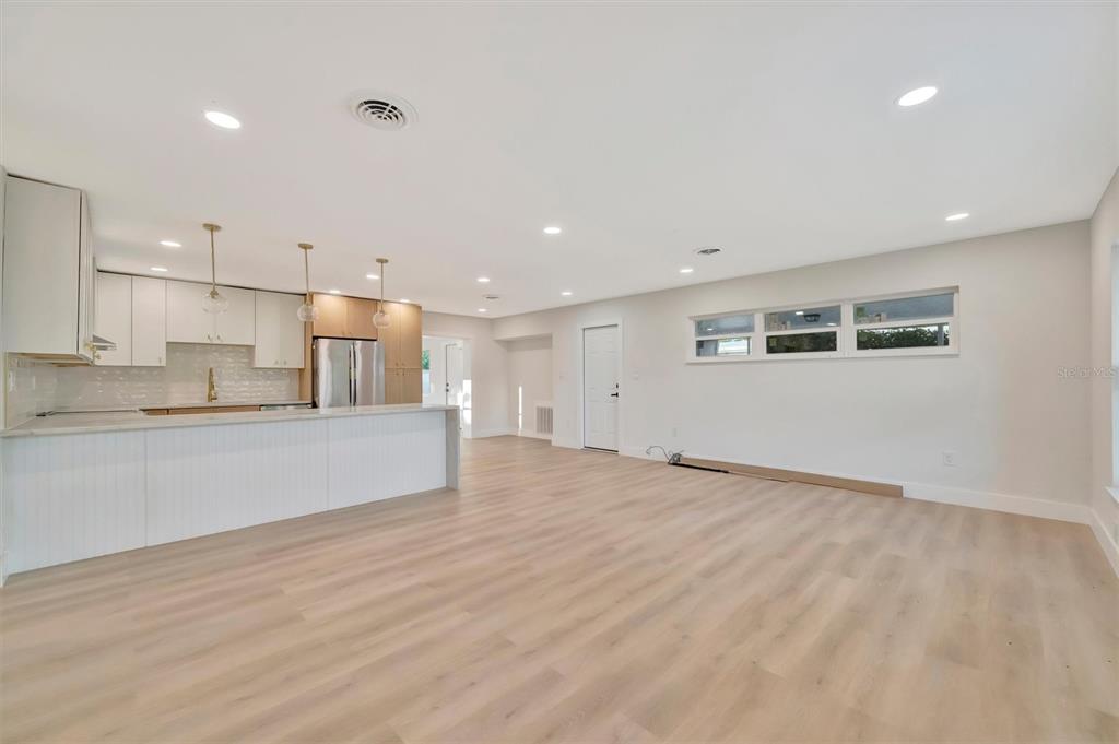 An open-concept kitchen and living area features light wood flooring and white cabinetry — 2705 SUNNYSIDE STREET, SARASOTA, FL