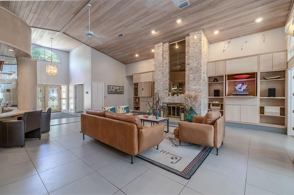 A spacious living room features a stone fireplace, wood-paneled ceiling, and light-colored tile flooring — 101 N ST ANDREWS DRIVE, ORMOND BEACH, FL