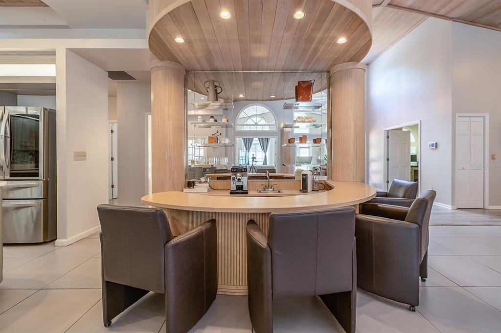 A curved bar with leather chairs sits beneath a wood-paneled ceiling in a modern kitchen — 101 N ST ANDREWS DRIVE, ORMOND BEACH, FL