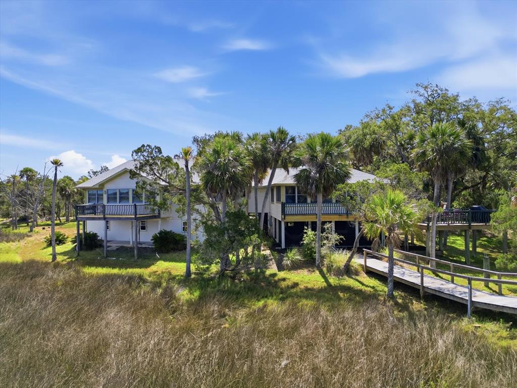 An elevated house with a wooden walkway sits surrounded by palm trees and tall grass — 12350 W RED MAPLE STREET, HOMOSASSA, FL