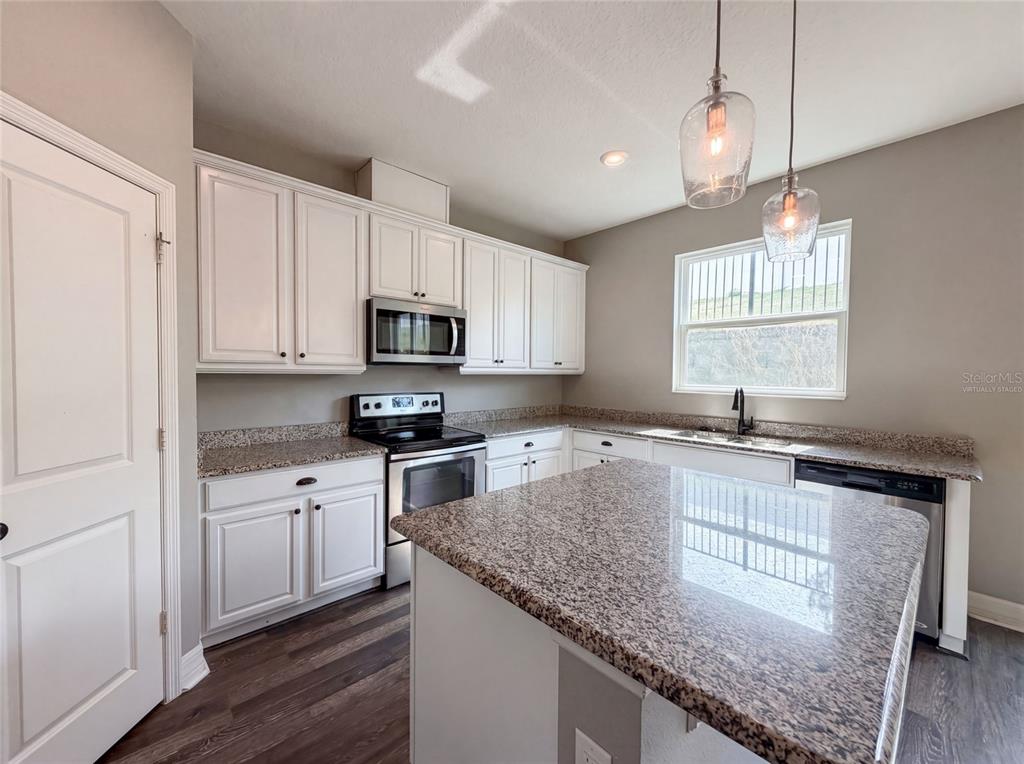 A kitchen features white cabinets, granite countertops, a center island, and stainless steel appliances — 10029 WEATHERS LOOP, CLERMONT, FL