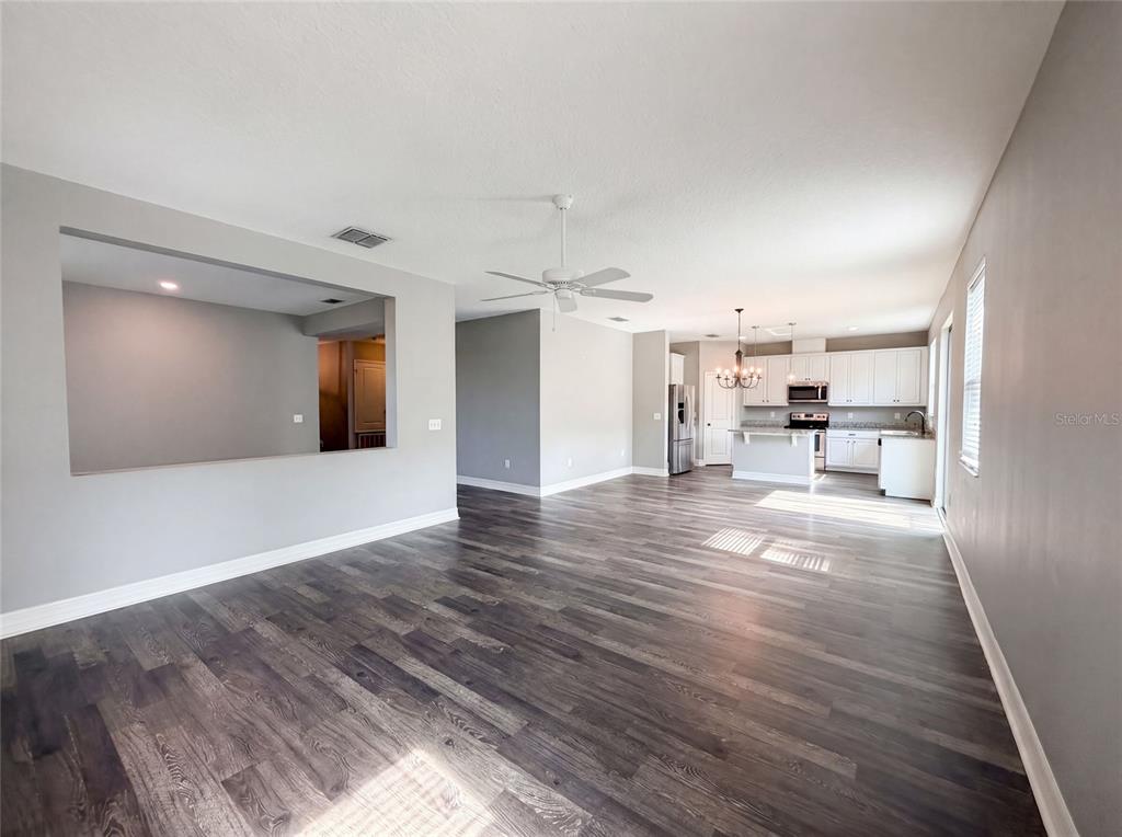 An open-concept living area features dark wood-look flooring, gray walls, and a white kitchen — 10029 WEATHERS LOOP, CLERMONT, FL