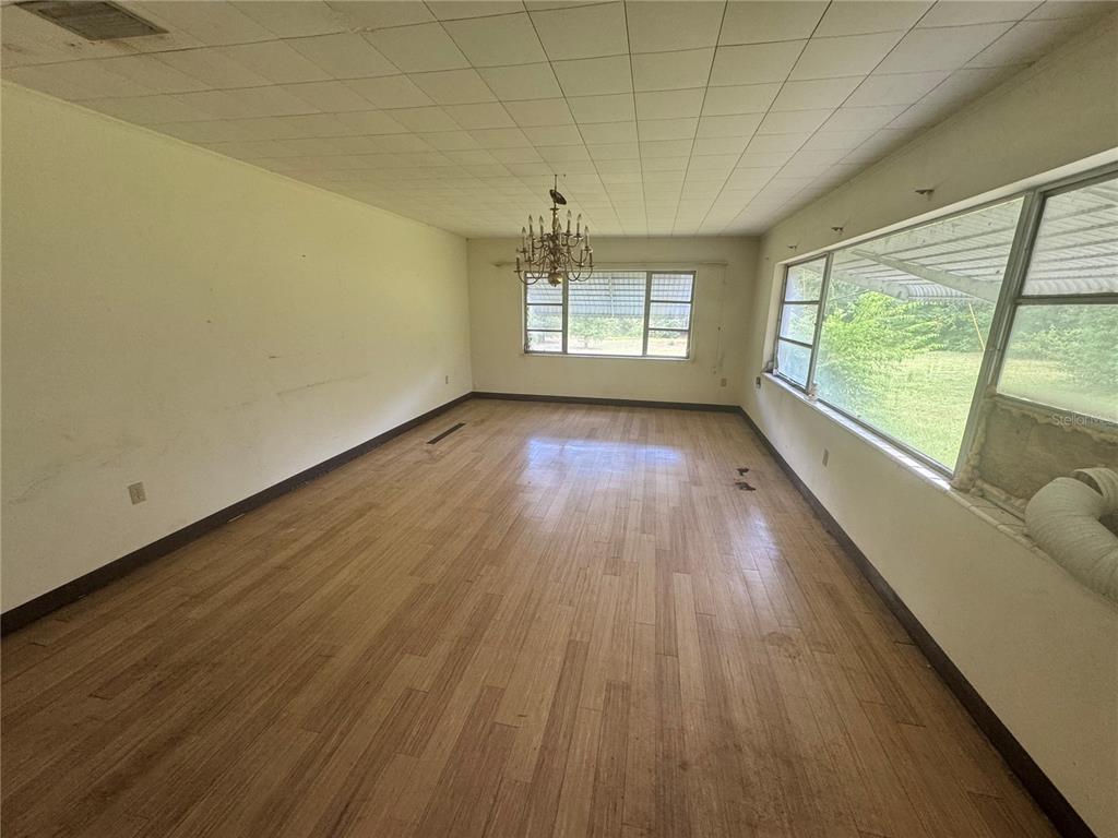 An empty room with light wood-look flooring, a grid-patterned ceiling, and large windows — 6187 OGBURN STREET, BROOKSVILLE, FL
