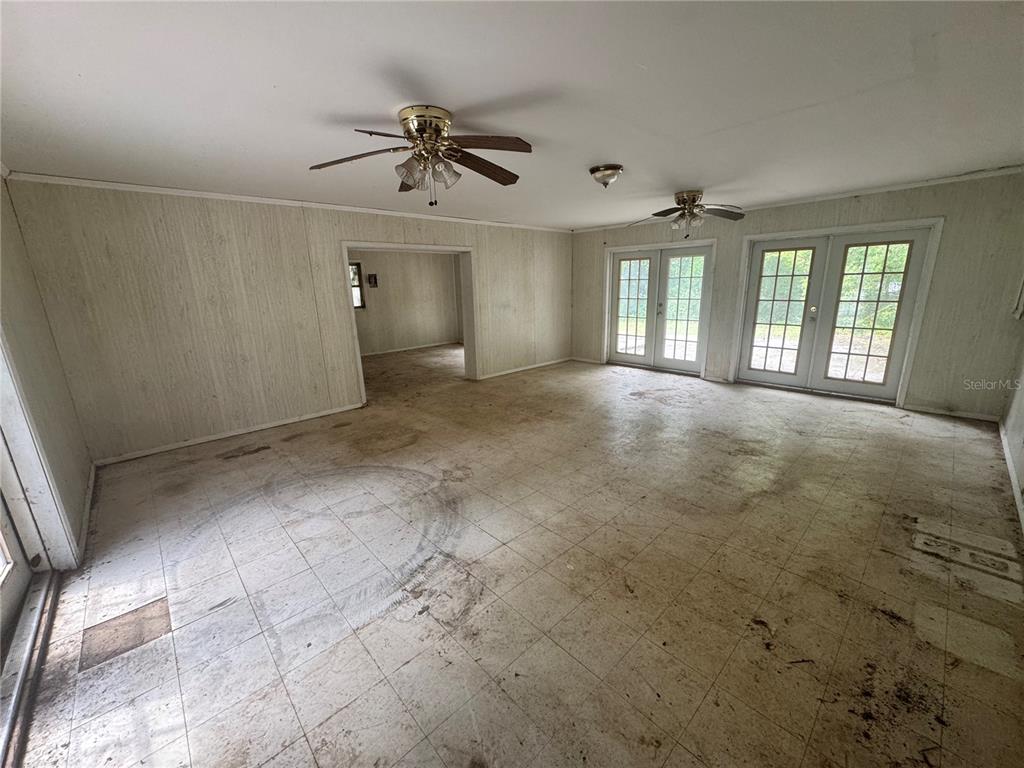 A large, empty room features wood-paneled walls, tiled flooring, two ceiling fans, and French doors — 6187 OGBURN STREET, BROOKSVILLE, FL