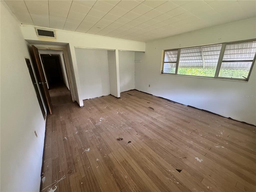 An empty room features wood-look flooring, white walls, a drop ceiling, and a large window — 6187 OGBURN STREET, BROOKSVILLE, FL
