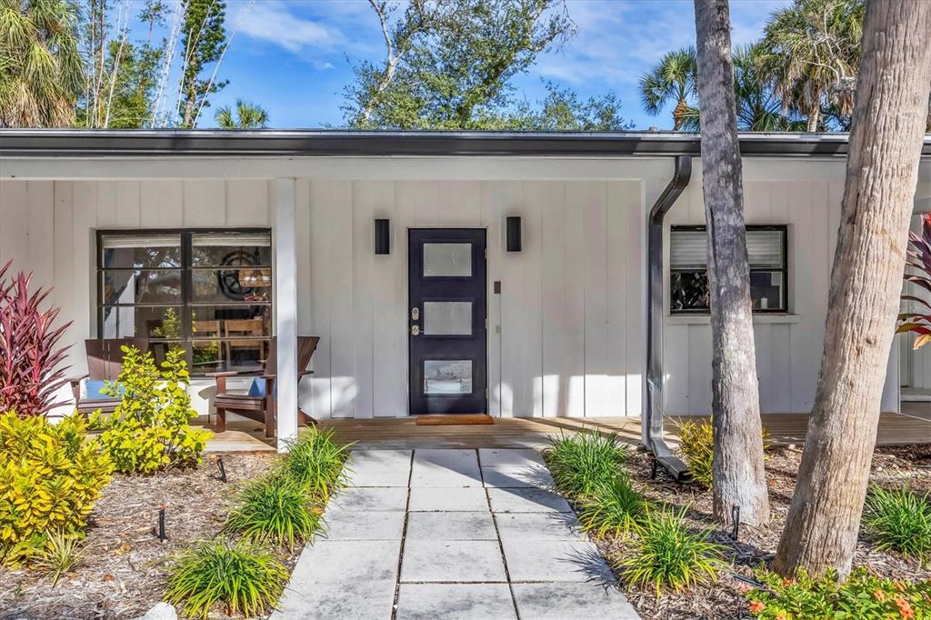 A white house exterior features a dark front door, a wooden porch, and a walkway — 445 REID STREET, SARASOTA, FL