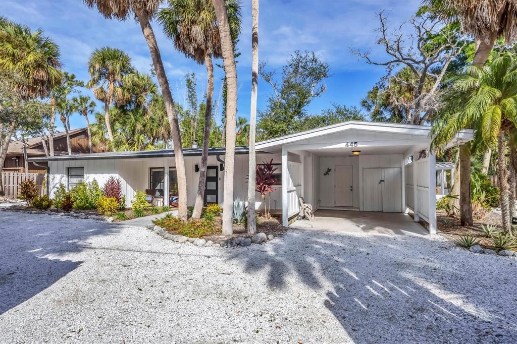 A white single-story house with a gravel driveway, carport, and palm trees in the yard — 445 REID STREET, SARASOTA, FL