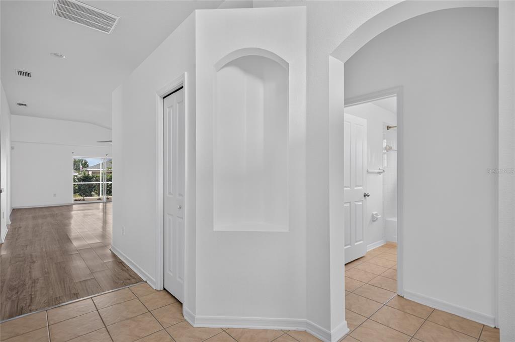 An empty room features dark wood-look flooring, white walls, a ceiling fan, and a window — 6833 RUNNER OAK DRIVE, ZEPHYRHILLS, FL