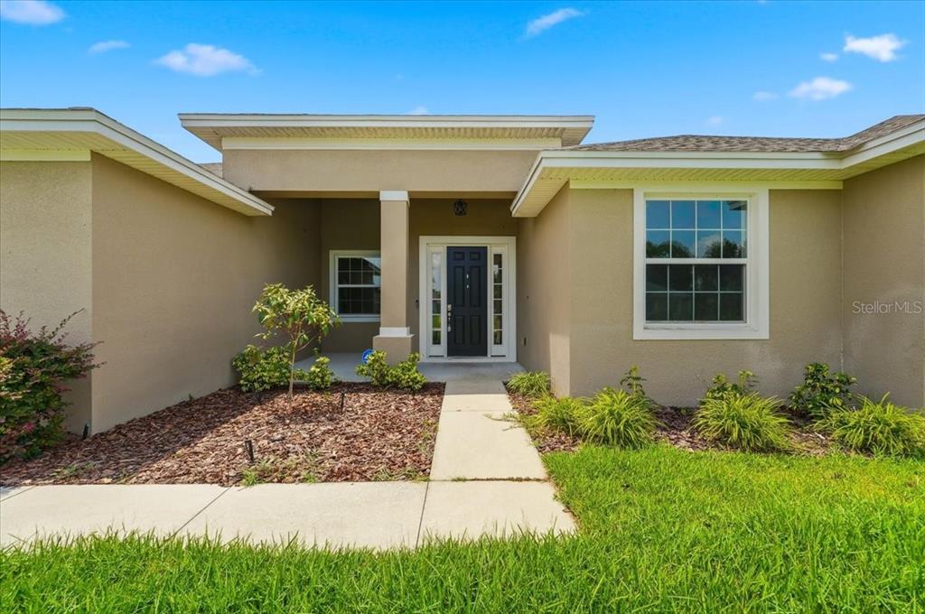 The exterior of a tan house features a covered entryway, a dark door, and landscaping — 5071 MOSS HAMMOCK TRAIL, SEBRING, FL