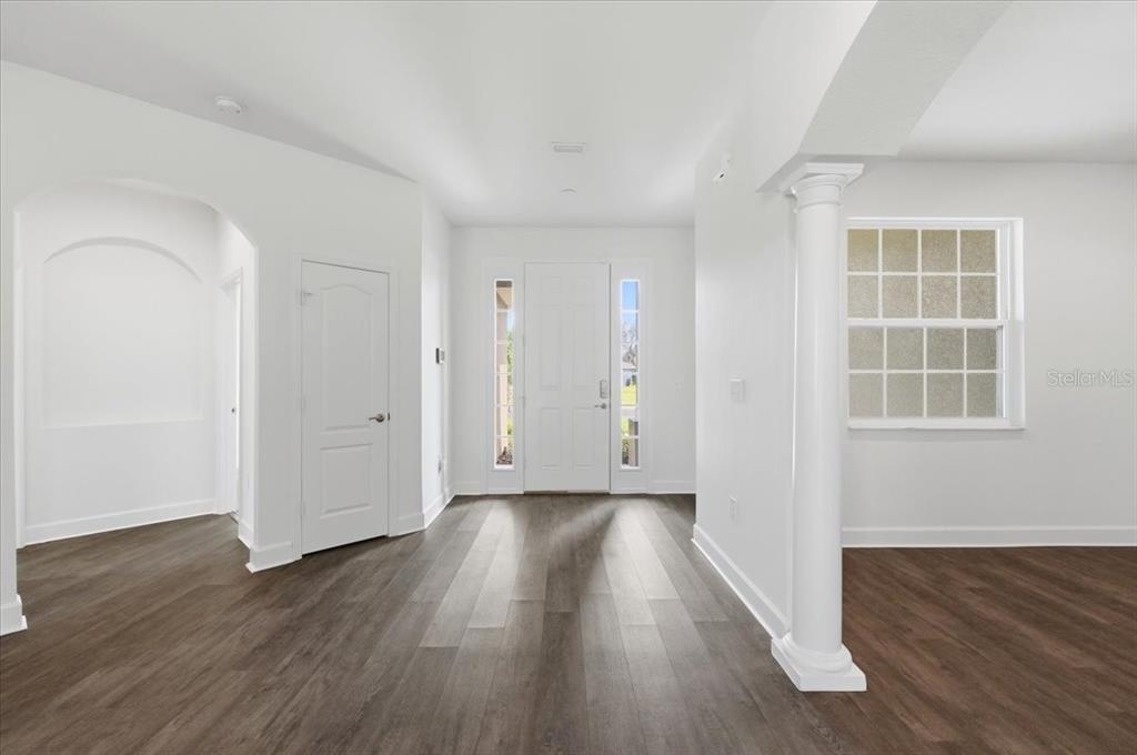 An entryway with white walls, dark wood-look flooring, a front door, and a decorative pillar — 5071 MOSS HAMMOCK TRAIL, SEBRING, FL