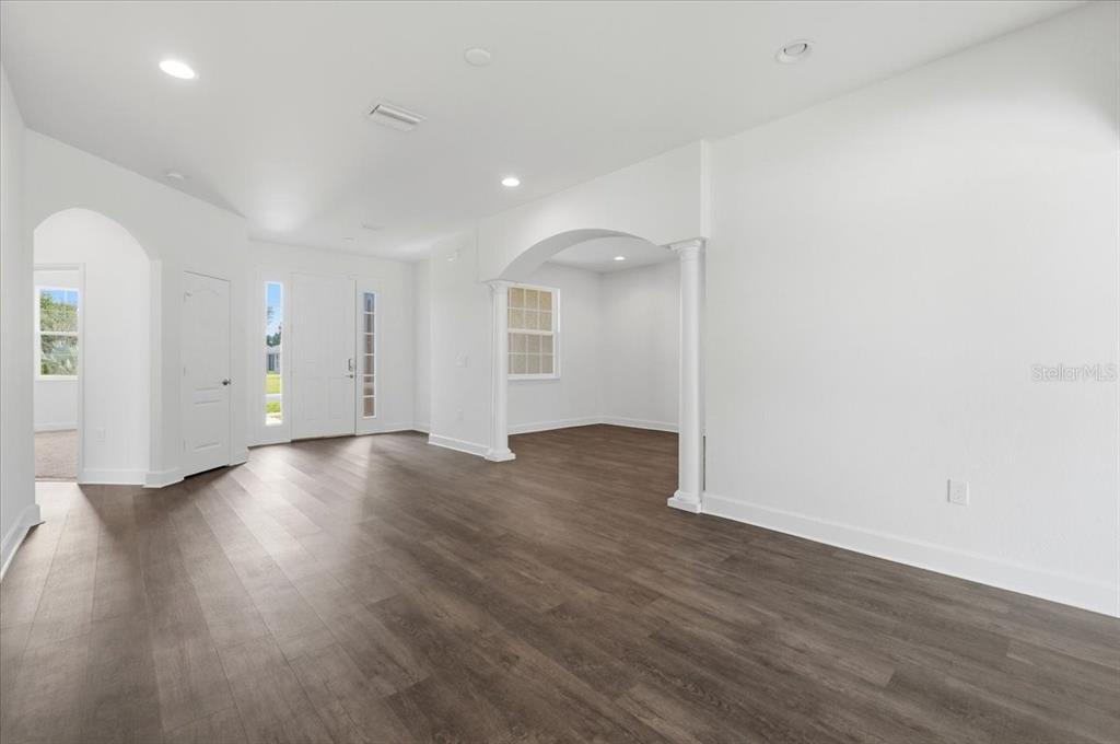 A bright, empty room features white walls, dark wood-look flooring, and an arched entryway — 5071 MOSS HAMMOCK TRAIL, SEBRING, FL