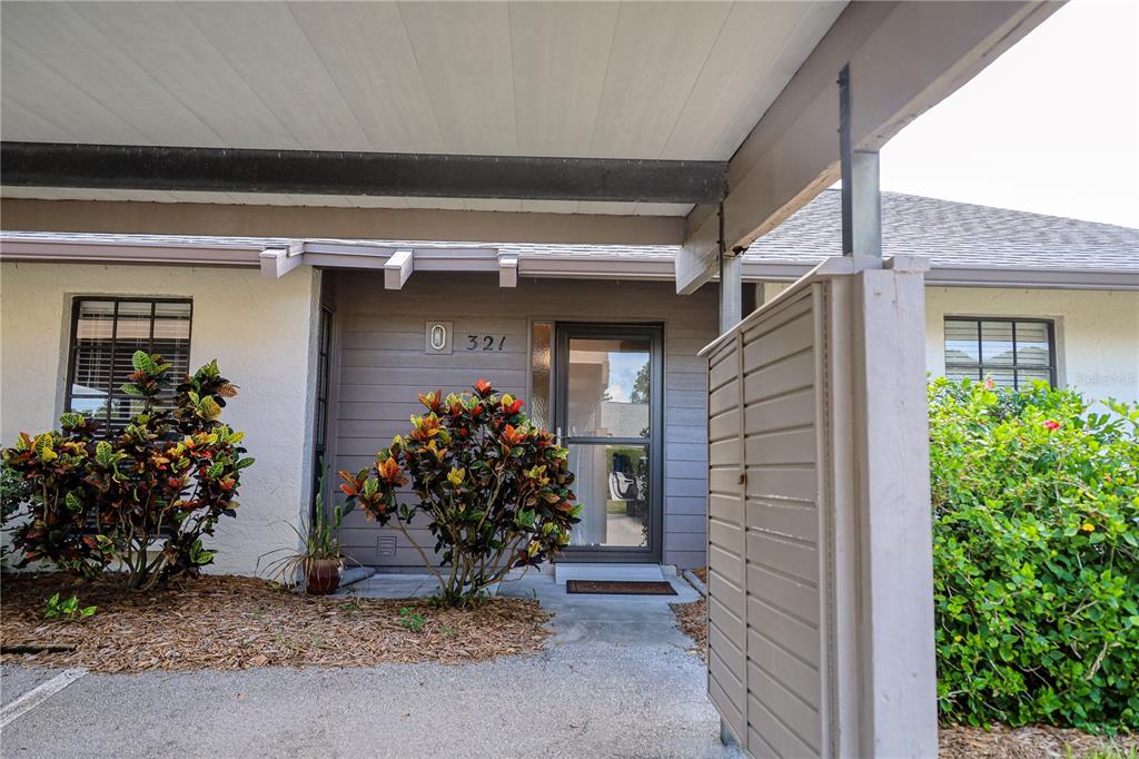 An exterior view of a residential entrance with a covered walkway and colorful landscaping — 321 WINDRUSH LOOP, TARPON SPRINGS, FL