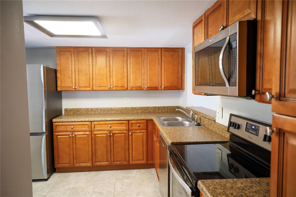 A kitchen features wood cabinets, granite countertops, stainless steel appliances, and a double basin sink — 321 WINDRUSH LOOP, TARPON SPRINGS, FL