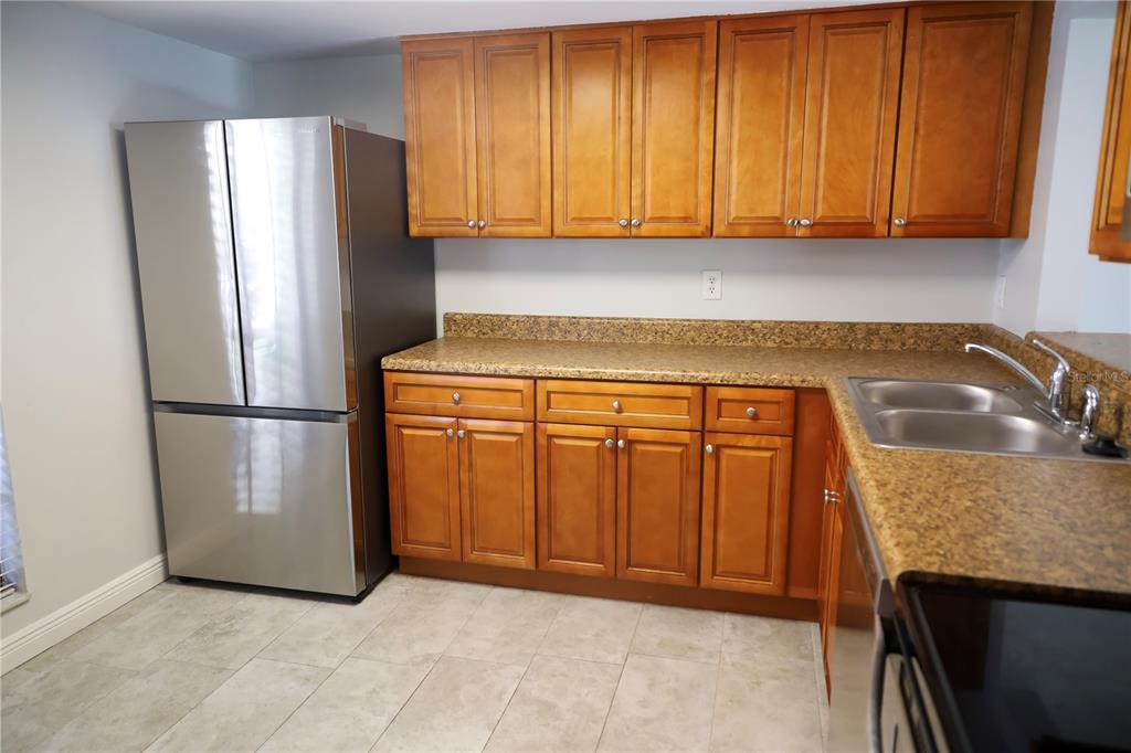 A kitchen features wood cabinets, granite countertops, a stainless steel refrigerator, and light tile flooring — 321 WINDRUSH LOOP, TARPON SPRINGS, FL