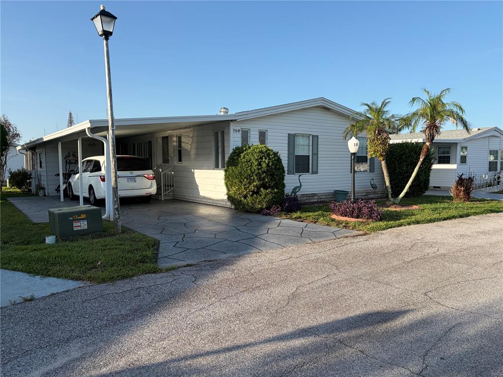 A single-story mobile home with a carport, driveway, and palm trees in a residential neighborhood — 260 RAMSGATE WAY, HAINES CITY, FL