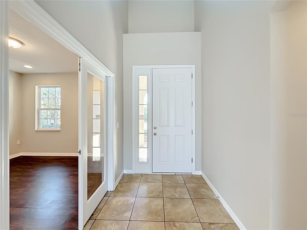 An entryway with tiled flooring, a white front door, and a glass-paneled door to a room — 3319 BETHPAGE LOOP, MOUNT DORA, FL