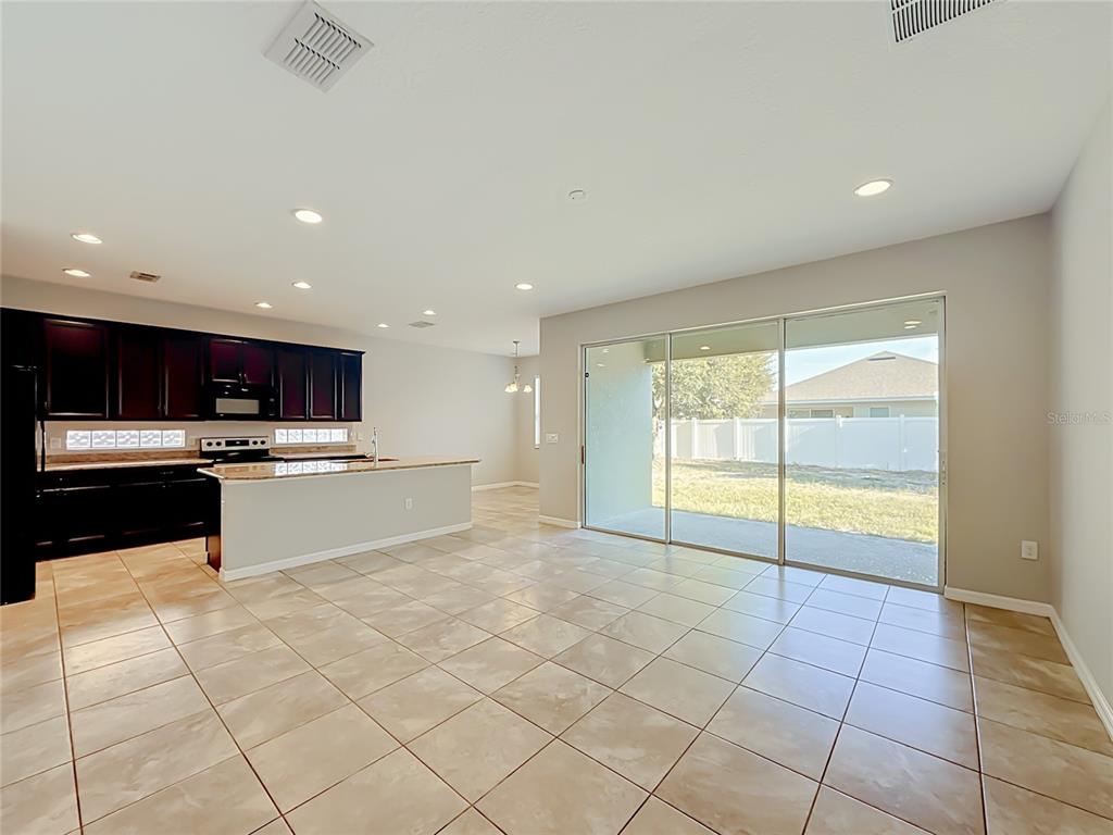 An open-concept kitchen with dark cabinets and tile flooring flows into a living area — 3319 BETHPAGE LOOP, MOUNT DORA, FL