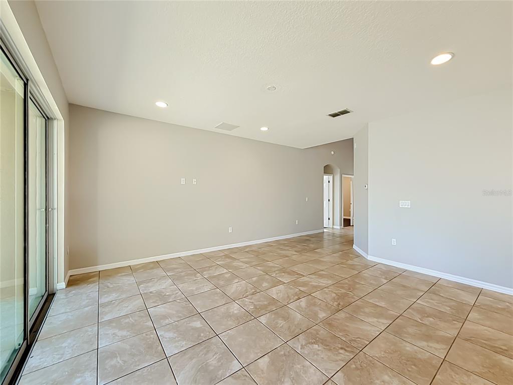 An empty living room features beige walls, large floor tiles, and a sliding glass door — 3319 BETHPAGE LOOP, MOUNT DORA, FL