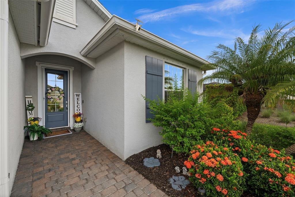 A paved walkway leads to the front entrance of a house with a blue door — 43047 PARKSIDE COURT, PUNTA GORDA, FL