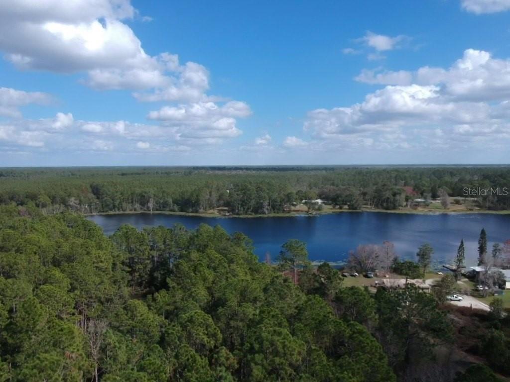 An aerial view shows a lake surrounded by dense forest under a blue sky — 0 Gracie DRIVE, PAISLEY, FL