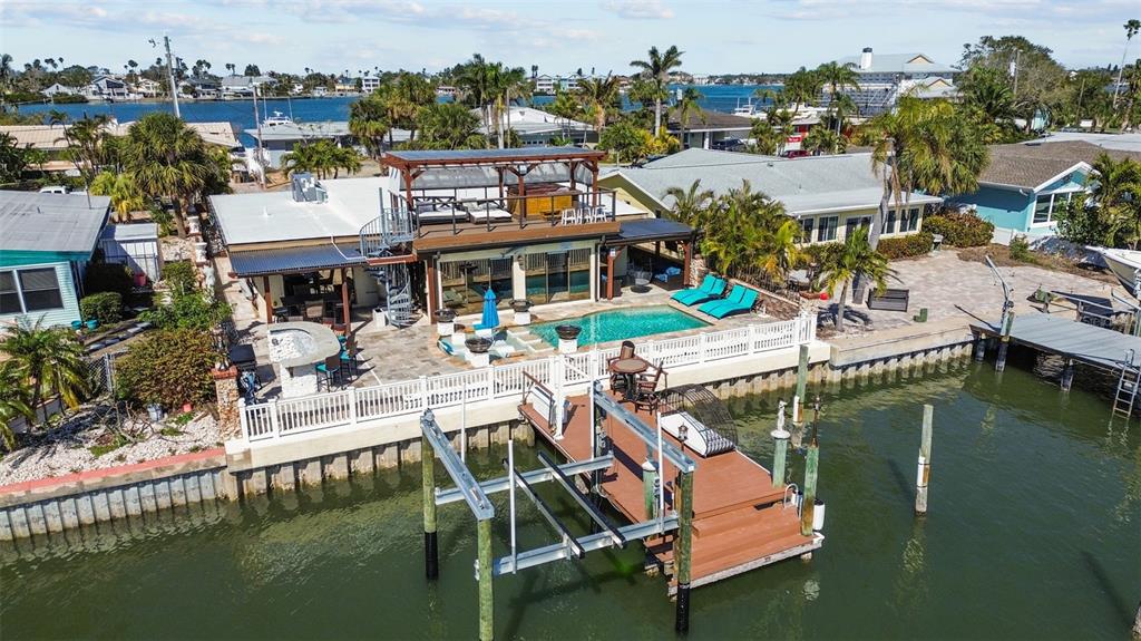 A waterfront patio features a swimming pool with lounge chairs and decorative stone water bowls — 357 LA HACIENDA DRIVE, INDIAN ROCKS BEACH, FL