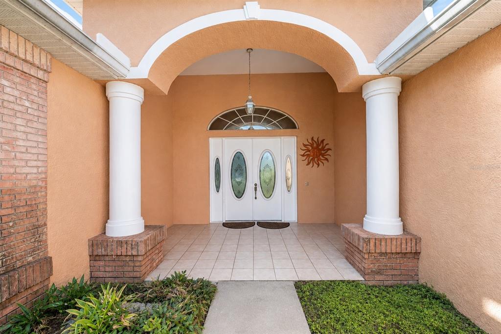 A covered front porch features white double doors with glass inserts and two large columns — 13566 RUDI LOOP, SPRING HILL, FL