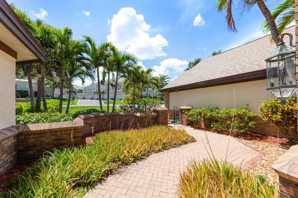 A brick walkway leads toward a house entrance past a low brick wall and landscaping — 280 BELLEVIEW BOULEVARD, BELLEAIR, FL