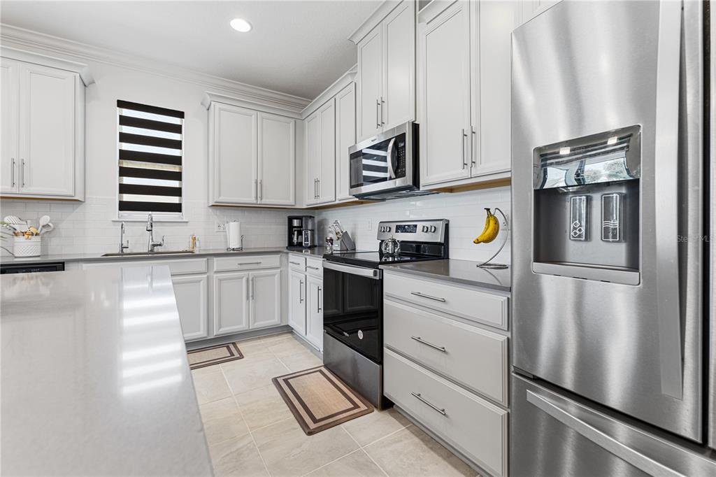 A modern kitchen features light gray cabinets, stainless steel appliances, and a large island — 3399 SAGEBRUSH STREET, HARMONY, FL