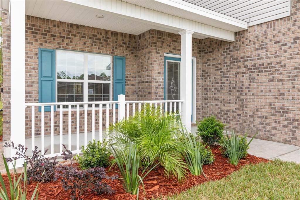 A brick house exterior features a covered front porch with white railings and blue shutters — 9 SQUIRREL PLACE, PALM COAST, FL