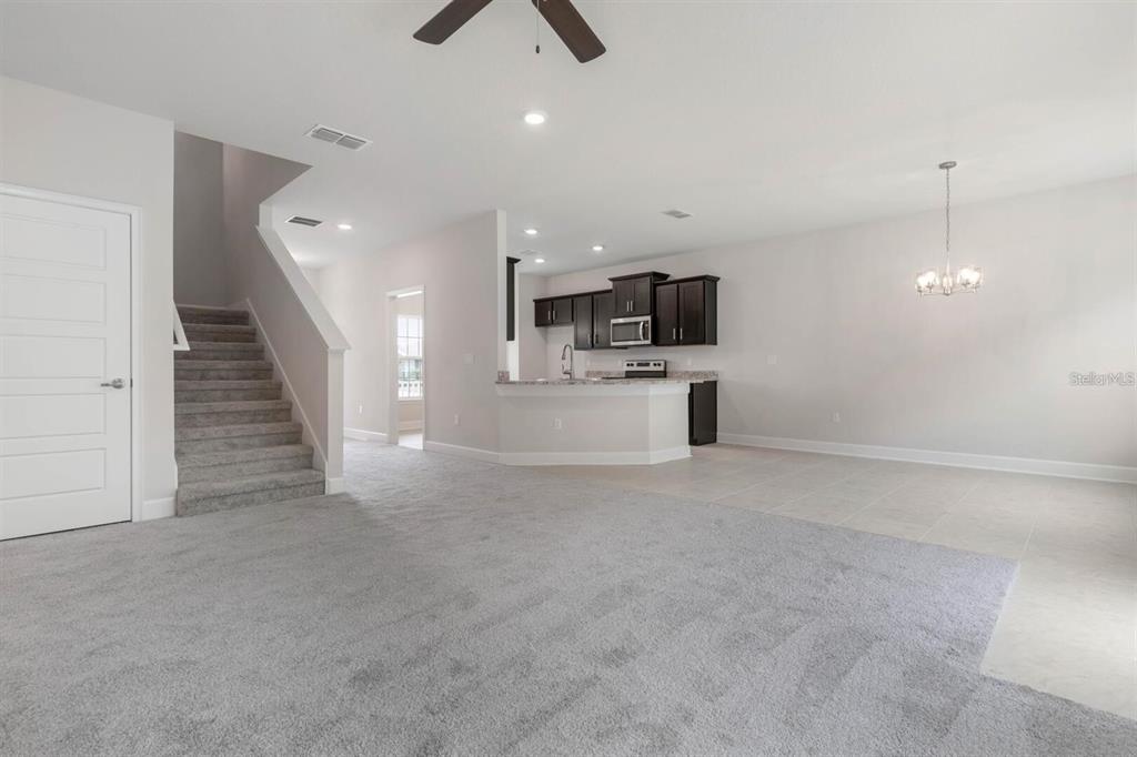 An open-concept living area features gray carpeting, a staircase, and a kitchen with dark cabinets — 9 SQUIRREL PLACE, PALM COAST, FL