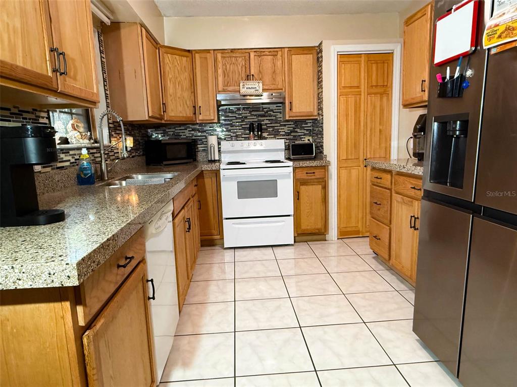 A kitchen features light wood cabinets, granite countertops, white appliances, and a tiled floor — 620 GLENDALE STREET, STARKE, FL