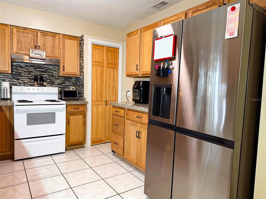A kitchen features wood cabinets, a white stove, a stainless steel refrigerator, and tiled floors — 620 GLENDALE STREET, STARKE, FL