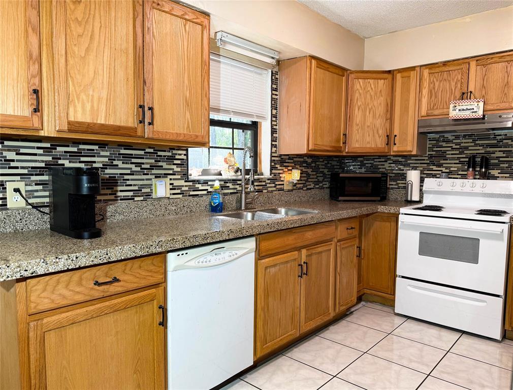 A kitchen features oak cabinets, granite countertops, a tiled backsplash, and white appliances — 620 GLENDALE STREET, STARKE, FL
