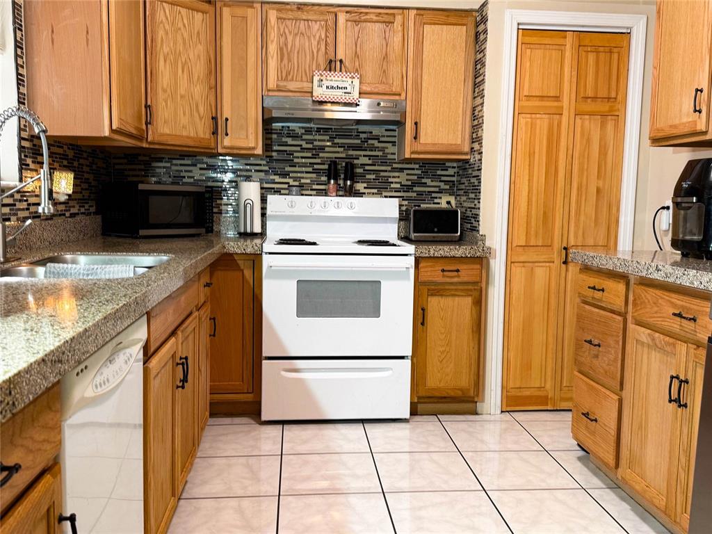 A kitchen features wood cabinets, granite countertops, a white stove, and a tiled backsplash — 620 GLENDALE STREET, STARKE, FL