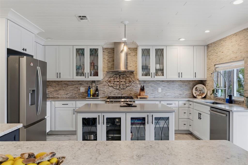 A modern kitchen features white cabinetry, a central island, stainless steel appliances, and stone backsplash — 137 12TH STREET E, TIERRA VERDE, FL
