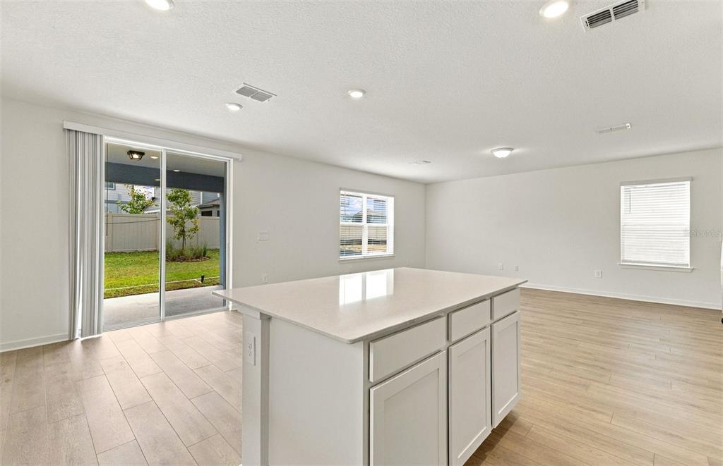 A kitchen features brown cabinets, a white speckled island, stainless steel appliances, and pendant lighting — 1543 HARTRIDGE COURT, LAKE ALFRED, FL