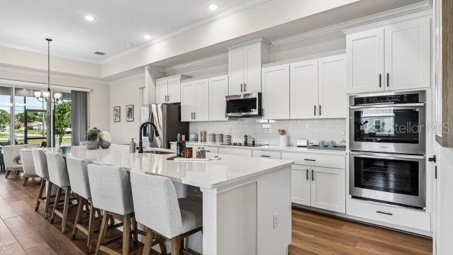A modern kitchen features white cabinetry, a large quartz island with seating, and stainless steel appliances — 5017 N PEPPERMINT DRIVE, BEVERLY HILLS, FL