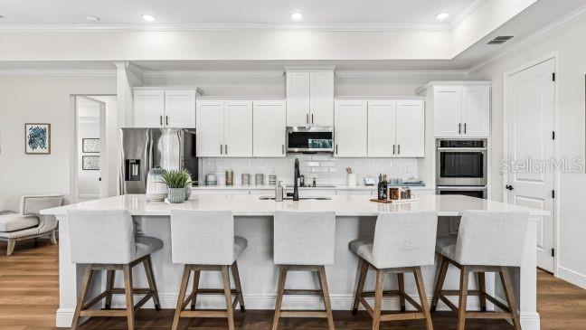 A modern kitchen features white cabinetry, a large island with four stools, and stainless appliances — 5017 N PEPPERMINT DRIVE, BEVERLY HILLS, FL