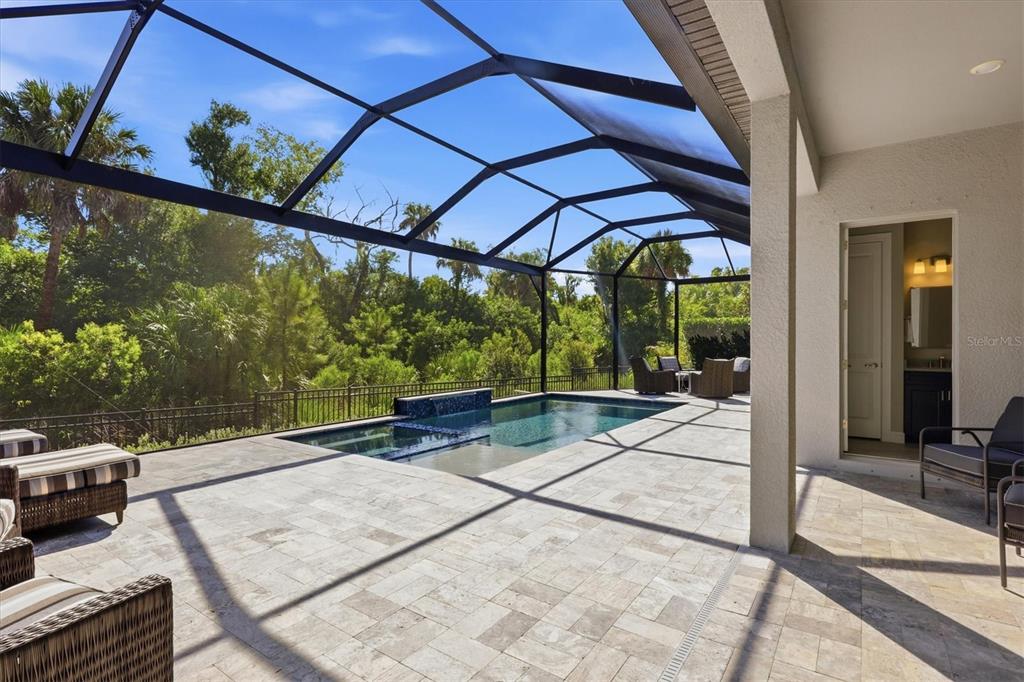 A screened-in patio features a swimming pool, stone pavers, and a view of lush trees — 10708 SARATOGA PLACE, PARRISH, FL