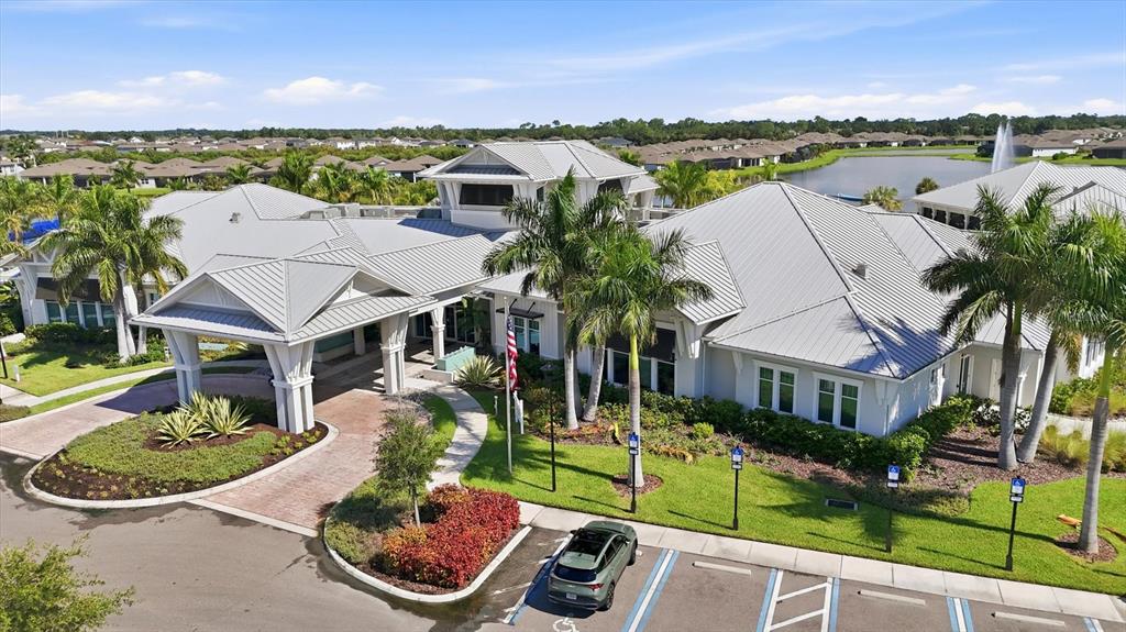 An aerial view shows a large clubhouse with a metal roof, palm trees, and parking — 10708 SARATOGA PLACE, PARRISH, FL