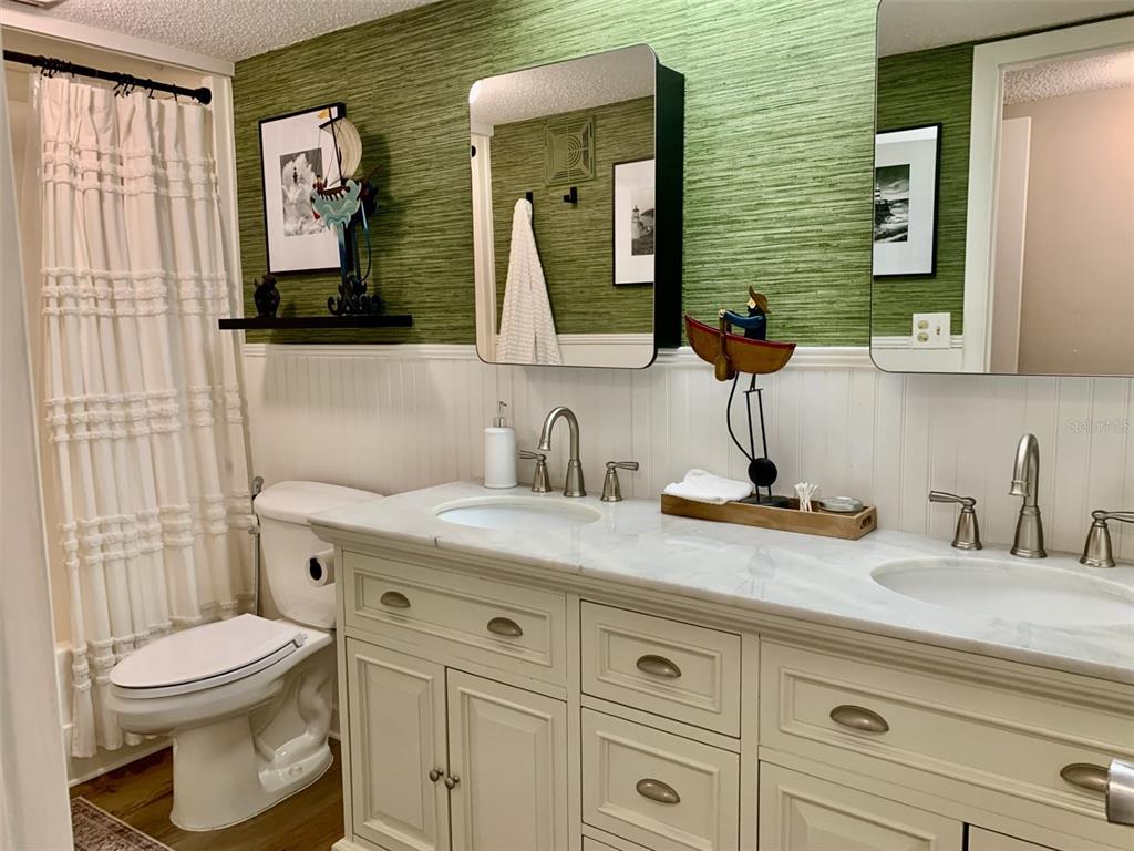 A bathroom features a double vanity with marble countertop, green textured wallpaper, and white wainscoting — 1655 S HIGHLAND AVENUE UNIT I379, CLEARWATER, FL