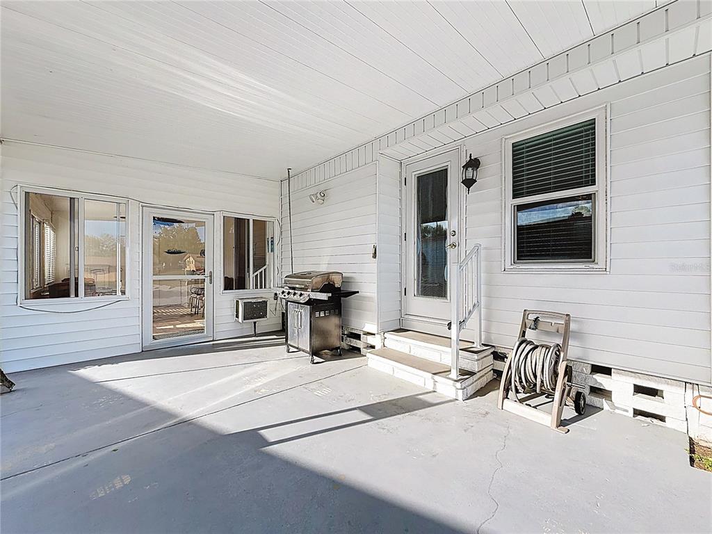 A covered patio features white siding, a grill, a hose reel, and two entry doors — 10184 106TH AVENUE UNIT 26, LARGO, FL