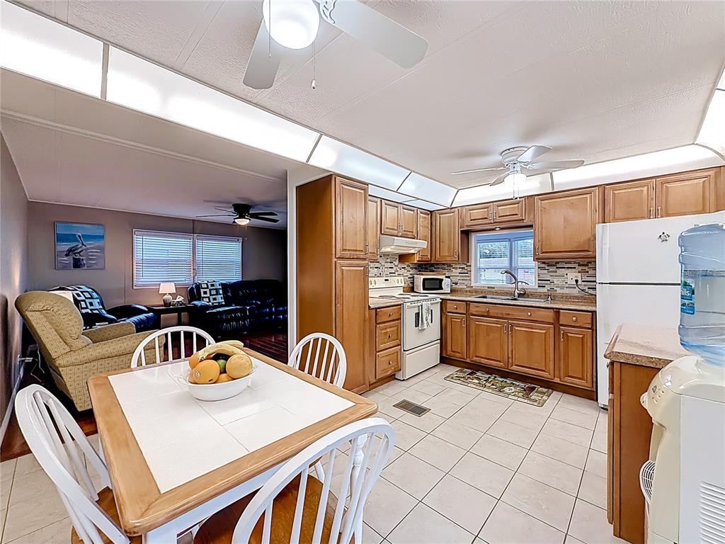 A kitchen with wood cabinets and tile floors opens to a dining area and living room — 10184 106TH AVENUE UNIT 26, LARGO, FL