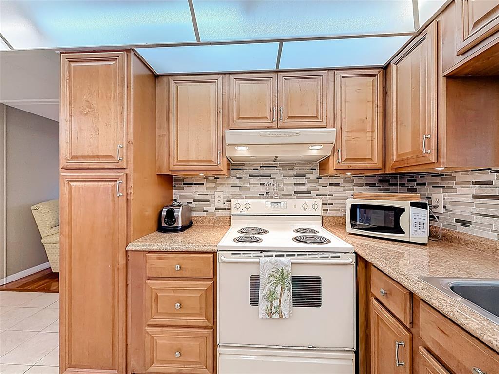 A kitchen features wood cabinets, a white stove, a microwave, and a tiled backsplash — 10184 106TH AVENUE UNIT 26, LARGO, FL