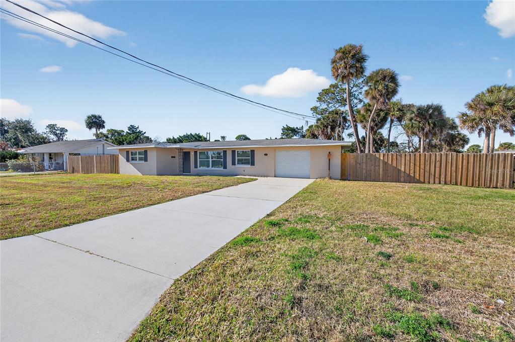 A single-story house with a concrete driveway, a white garage door, and a wooden fence — 123 W OCEAN AVENUE, EDGEWATER, FL