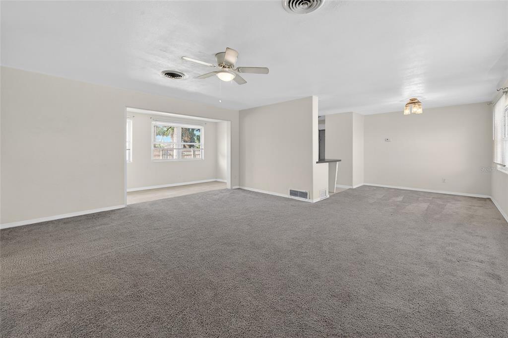 A spacious, carpeted living room features a ceiling fan, neutral walls, and an adjacent dining area — 123 W OCEAN AVENUE, EDGEWATER, FL