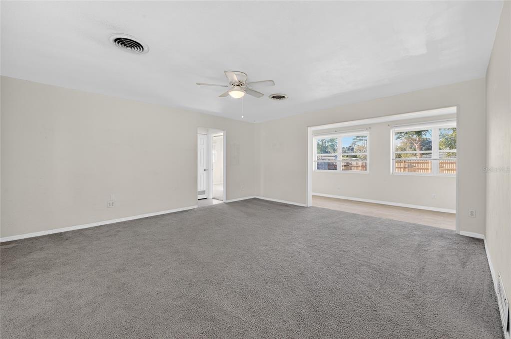 A spacious living room with gray carpeting, a ceiling fan, and a large windowed alcove — 123 W OCEAN AVENUE, EDGEWATER, FL